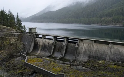A concrete spillway dam holding back a long forested reservoir under low mist (AI-generated image)
