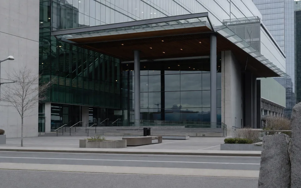 A glass-and-concrete conference building with a deep entrance canopy above an empty plaza on a downtown street (AI-generated image)